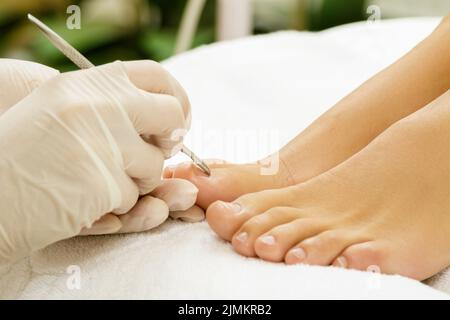 Pedicure lavoro maestro. Primo piano di unghie e mani femminili nei guanti con uno speciale utensile in acciaio. Foto Stock