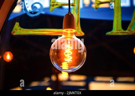 Una grande lampadina rotonda a incandescenza di colore giallo caldo appende al soffitto in un bar Foto Stock