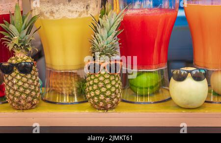 Papaya fresca, cocomero, ananas e succhi di frutta mango decorati con ananas e occhiali da sole al mercato. Succhi di frutta colorati. Nessuno Foto Stock