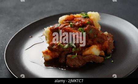 Stufato di manzo con salsa di pomodoro, spezie ed erbe aromatiche su purè di patate. Foto Stock