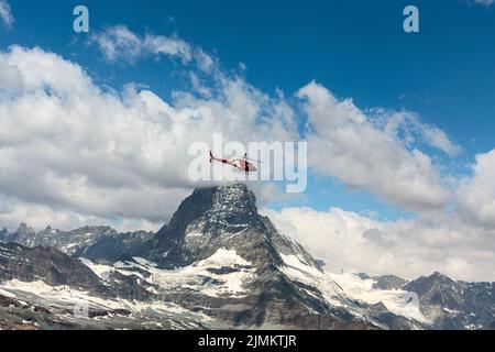 Cervino nelle Alpi svizzere. Una nuvola bianca si trova sulla montagna. Un elicottero di sorveglianza rosso vola sopra di esso. Foto Stock