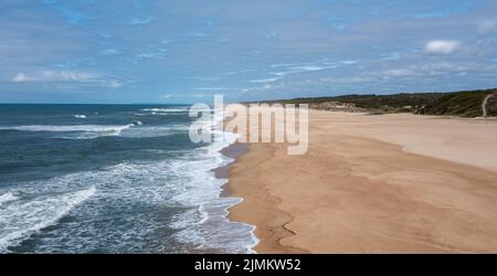 Vista da un drone di un'ampia e infinita spiaggia di sabbia dorata con alte dune di sabbia e vegetazione dietro Foto Stock