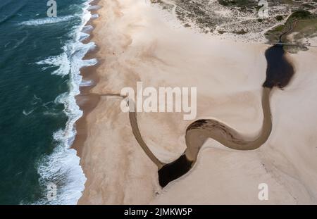 Vista mozzafiato di un'ampia e infinita spiaggia di sabbia dorata con un fiume che scorre verso l'oceano Foto Stock