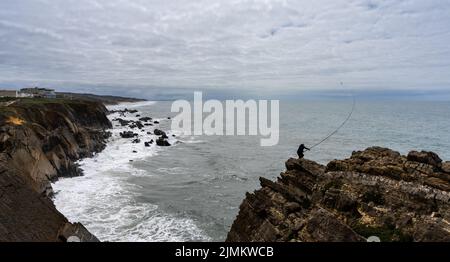 Pescatore pesca da una scogliera rocciosa sulla costa atlantica selvaggia del Portogallo settentrionale Foto Stock