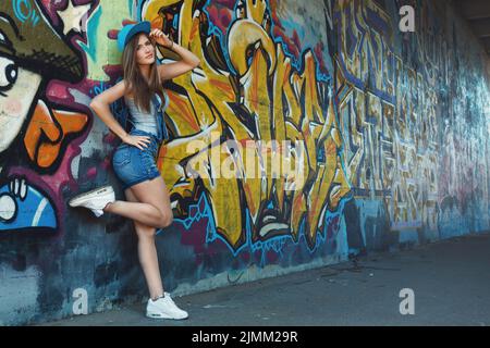 Ragazza in tuta denim che posa contro il muro con graffiti Foto Stock