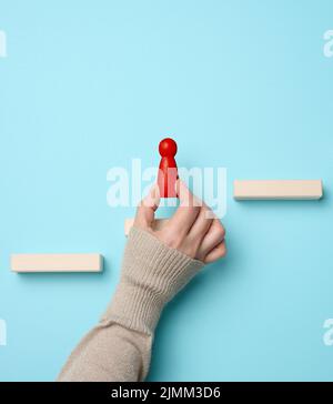 Gradini di legno e una figurina di un piccolo uomo in mano di una donna. Avvio, avvio di un nuovo business di successo, raggiungimento degli obiettivi Foto Stock