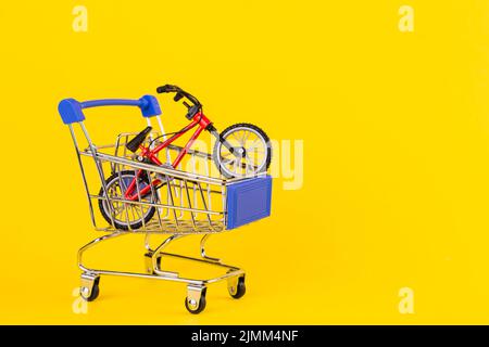 Piccolo carrello di shopping giocattolo per biciclette su sfondo giallo Foto Stock