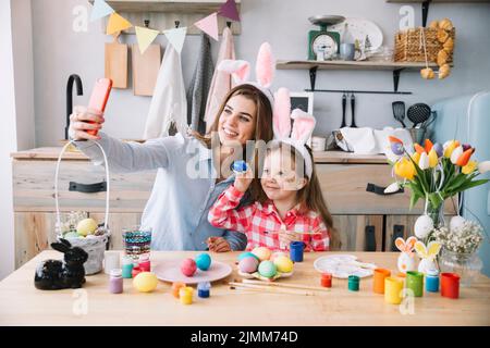 Donna che prende selfie con figlia vicino alle uova di pasqua Foto Stock