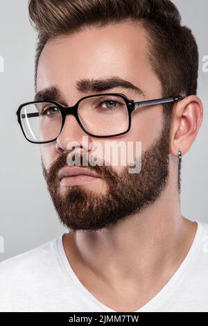 Uomo elegante barbuto in occhiali su sfondo grigio Foto Stock