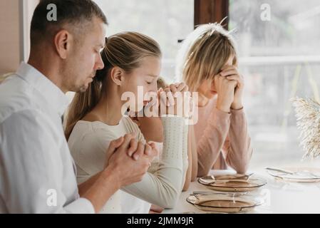 Bella famiglia che prega insieme prima di mangiare Foto Stock