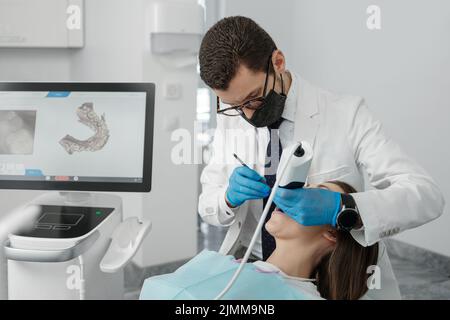 Paziente di lavaggio ortodontista maschile con scanner dentario intraorale e controlli processo sullo schermo. Concetto di protesi e stomatologia. Foto Stock