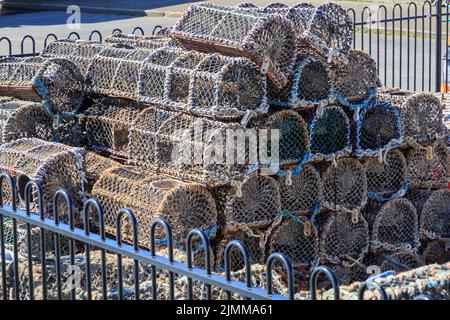 Impila di vasi di aragosta in un composto recintato sulla parete del porto Foto Stock