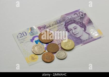 Banconote e monete in sterline britanniche da venti sterline in primo piano su bianco. Ritratto se la regina Elisabetta II. Foto Stock