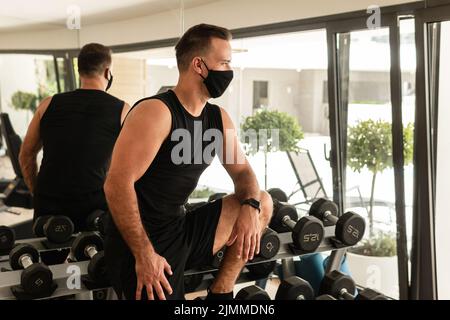 Giovane atletico che indossa una maschera facciale di prevenzione durante il suo allenamento in palestra Foto Stock