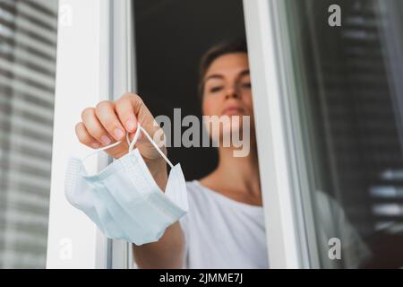Donna gettando via la maschera di prevenzione usata. Simbolo della fine della pandemia. Foto Stock