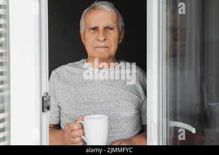 Uomo anziano con una tazza di caffè che guarda alla finestra Foto Stock