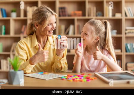 Il terapista amichevole di discorso che cura i problemi del bambino, ragazza carina che impara le lettere R e U con il tutor privato Foto Stock