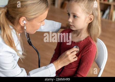 Medico femminile che controlla i polmoni del bambino durante il controllo medico, pediatra usando stetoscopio per esaminare il paziente piccolo Foto Stock