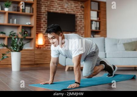 Uomo asiatico sportivo di mezza età che fa esercizio di running Plank, formazione su tappeto yoga a casa in soggiorno, spazio copia Foto Stock
