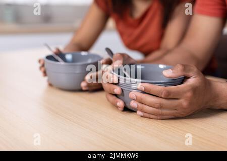 Cropped uomo e donna millennial afroamericano tengono in mano piatti vuoti al tavolo in cucina, primo piano Foto Stock