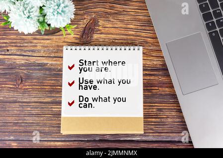 Controllare i messaggi motivazionali sul notebook sul tavolo con il laptop e decorazione floreale. Inizi dove yo sono, usi che cosa avete, faccia che cosa può. Foto Stock