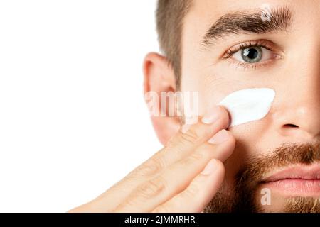 Giovane uomo sta applicando crema idratante e anti invecchiamento sul suo viso Foto Stock