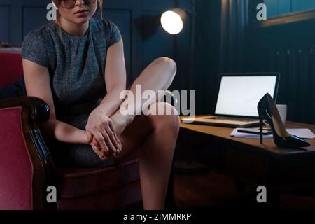 Donna d'affari con piedi doloranti dopo una lunga giornata lavorativa di indossare tacchi alti Foto Stock