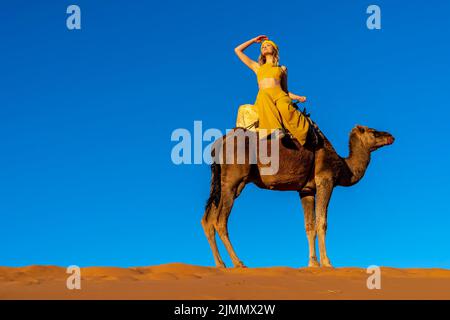 Una bella modella guida Un cammello dromedario attraverso il deserto del Sahara sui loro cammelli in Marocco Foto Stock