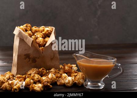 Popcorn caramellato in sacchetto di carta su tavolo da cucina in legno Foto Stock