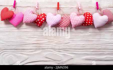 Cuori di tessuto valentini appesi su corda su sfondo bianco di legno Foto Stock