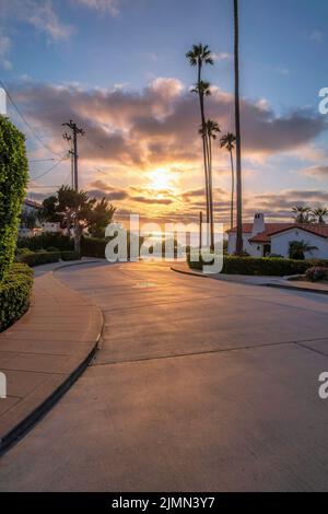Vista al tramonto sull'oceano da una strada a la Jolla, California. Strada in cemento inclinata vicino alle case mediterranee, cespugli e pali elettrici Foto Stock