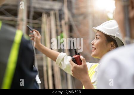 Ingegnere femminile asiatico che utilizza il lavoro di ordinazione radio presso il cantiere di costruzione Foto Stock