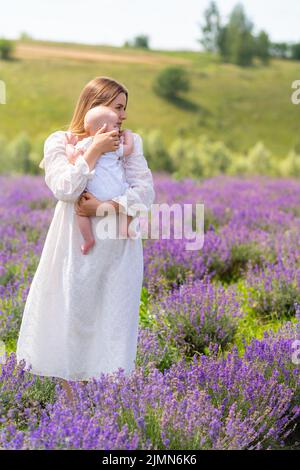 Giovane madre che cullava il suo piccolo bambino tra le braccia come si pone all'aperto in un campo di lavanda viola in estate Foto Stock