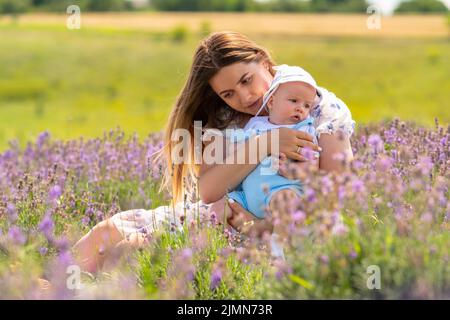 Madre con il suo figlio del bambino che gode un momento tranquillo insieme mentre si siedono distendendosi fra i fiori in un campo di lavanda Foto Stock