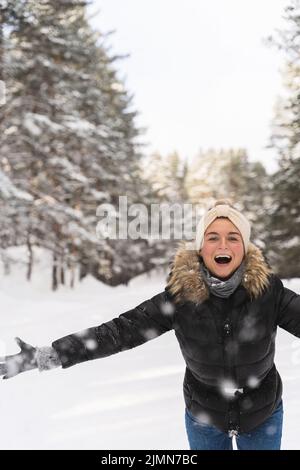 Donna allegra che getta la neve nell'aria durante la fredda giornata invernale Foto Stock