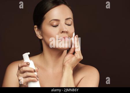 Bella donna di mezza età con un tampone di cotone e una bottiglia di liquido detergente Foto Stock