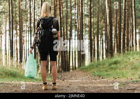 Escursionista femmina che raccoglie rifiuti di plastica nella foresta verde Foto Stock