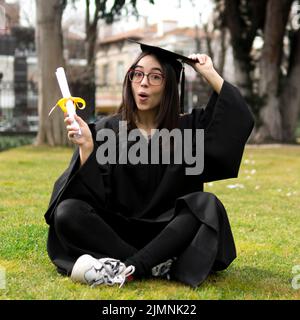 Cerimonia di laurea della giovane donna che tiene il cappello Foto Stock