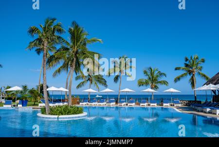 Splendido resort tropicale sulla spiaggia con piscina, lettini e palme durante una calda giornata di sole, paradiso de Foto Stock