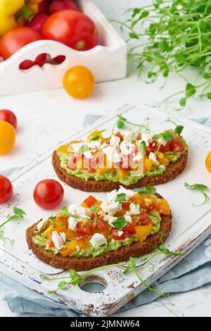 Toast all'avocado con feta e pomodori, scorribotta con ricotta, primo piano e verticale Foto Stock