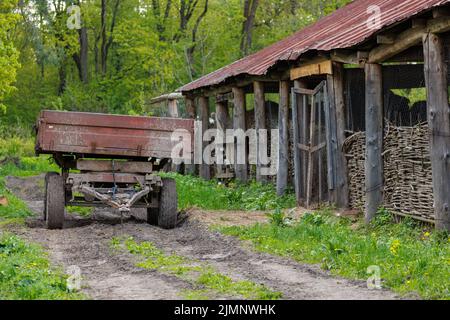 un vecchio rimorchio agricolo si trova accanto alle stalle in estate, primo piano con una messa a fuoco selettiva Foto Stock