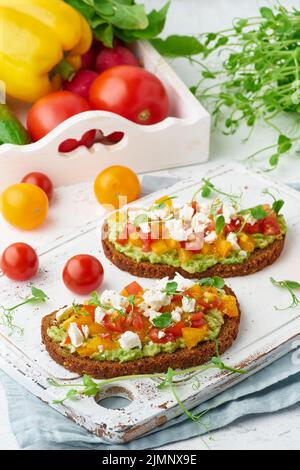 Toast all'avocado con feta e pomodori, scorribotta con ricotta, primo piano e verticale Foto Stock