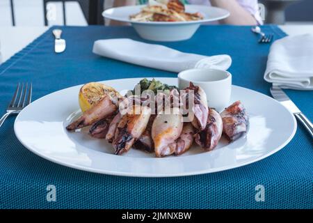 Calamari alla griglia con patate e spinaci su un piatto bianco. Piatto con frutti di mare. Cena romantica in un ristorante di pesce nella località del Montenegro. Viaggi Foto Stock