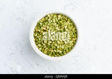 Piselli verdi in ciotola bianca su sfondo bianco. Cereali secchi in tazza, cibo vegano. Vista dall'alto, primo piano. Foto Stock