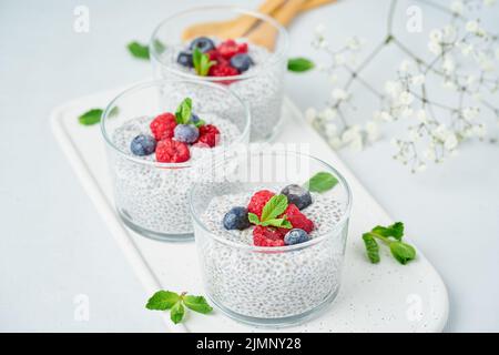 Budino di Chia con lamponi freschi di frutti di bosco, mirtilli. Tre vetri, sfondo chiaro, vista laterale, fiori. Foto Stock