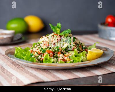 Insalata di tovouleh con quinoa. Cibo orientale con mix di verdure, dieta vegana. Vista laterale, tovagliolo di lino, vecchio piatto Foto Stock