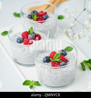 Budino di Chia con lamponi freschi di frutti di bosco, mirtilli. Tre vetri, sfondo chiaro, vista laterale, fiori, primo piano. Foto Stock