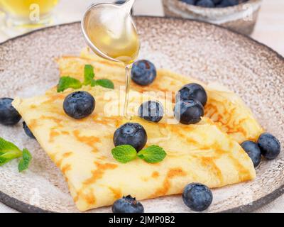 Due pancake con mirtilli e miele sul piatto, flussi di miele dal cucchiaio, vista laterale, primo piano Foto Stock