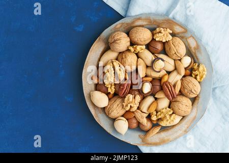 Blu classico nel cibo. Mix di noci sul piatto - noce, mandorle, noci pecan, macadamia Foto Stock