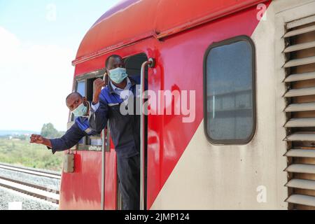 (220807) -- NAIROBI, 7 agosto 2022 (Xinhua) -- i conducenti keniani John Pius (L) e Brian Kemboi confermano la sicurezza con il personale della piattaforma alla stazione di Ngong a Kajiado, Kenya, 25 marzo 2022. Lanciato il 31 maggio 2017, il 480 km Mombasa-Nairobi Standard Gauge Railway (SGR), finanziato principalmente dalla Cina e costruito dalla China Road and Bridge Corporation (CRBC), ha favorito la creazione di posti di lavoro per la popolazione locale. Afristar, la società che opera la SGR, ha impiegato keniani in 123 professioni ferroviarie che rientrano sotto 5 dipartimenti ferroviari, compresi trasporto ferroviario, locomotiva, binario, segnale, e rotolare sto Foto Stock